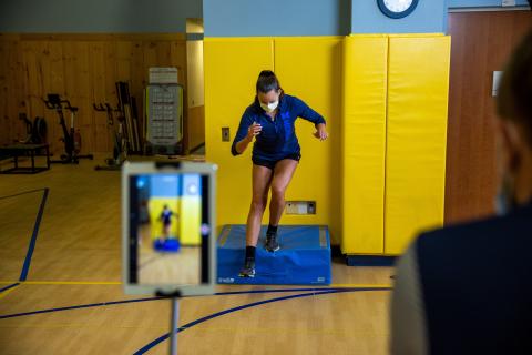 Woman wearing blue shirt practicing a move while a man records it.