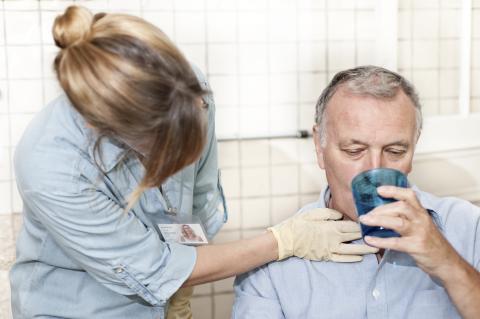 Healthcare worker checking man's throat as he drinks. 